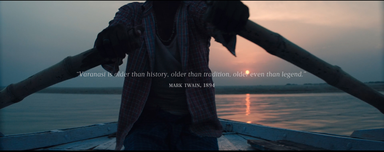 Zdjęcie to kadr z filmu, na którym człowiek przy zachodzącym słońcu, wiosłuje drewnianą łodzią.