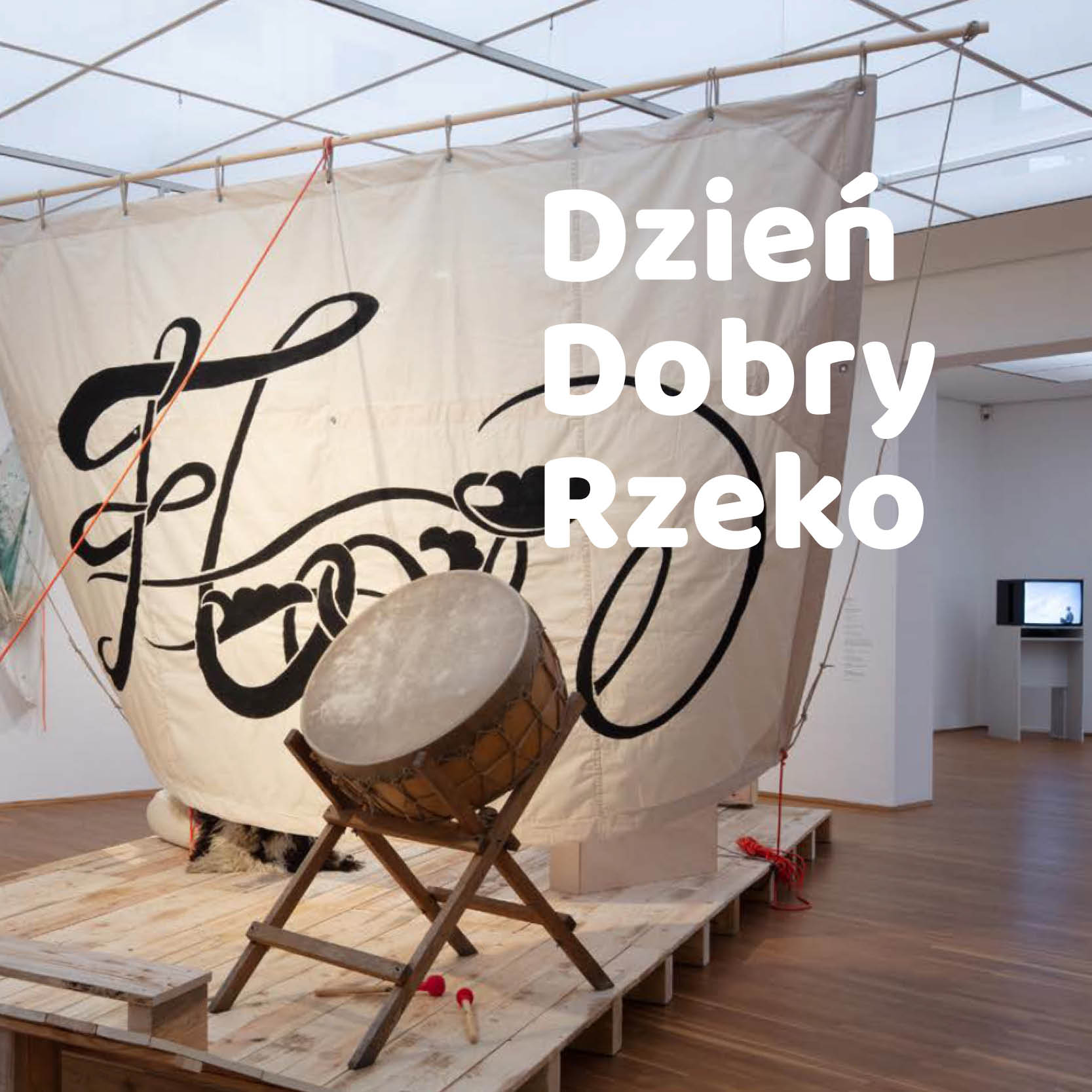 Zdjęcie Przedstawia galeryjną przestrzeń, w niej widać wiszący żagiel z napisem FLOW i wielki bęben stojący na drewnianej podłodze.