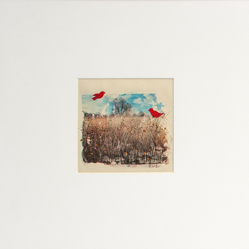 Obrazek przedstawiający pejzaż wczesnowiosenny. Na pierwszym planie wysokie wyrudziałe trawy. Na tle niebieskiego nieba rząd bezlistnych drzew z jednym wysokim, rozrośniętym, dominującym. Dodanym kolażowo elementem jest para czerwonych ptaków. W trawach pierwsze kwiatki (haft).
