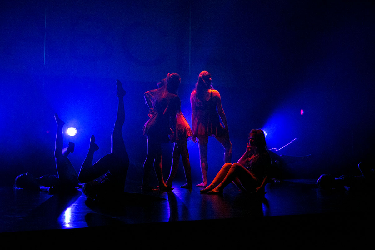 Na zdjęciu widoczne są tancerki na scenie teatralnej. Ciemne światło oraz przeważający kolor niebieski oświetlenia. 
