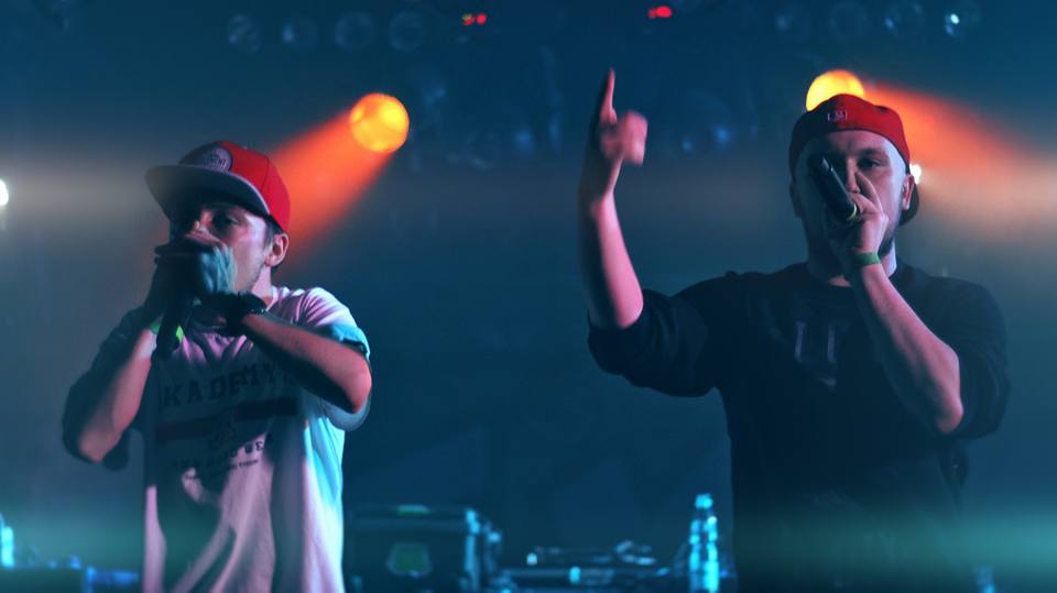 Na zdjęciu widoczne są dwie osoby trzymające mikrofony przy ustach. Obie osoby stoją na scenie.