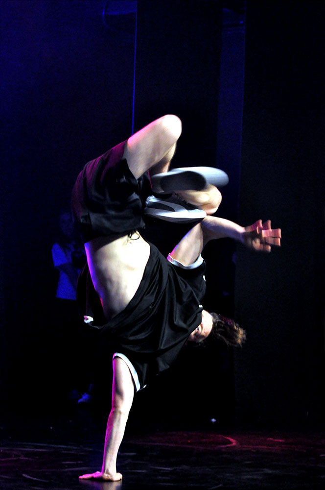 Na zdjęciu tancerz break dance stojący na jednej ręce na scenie. 