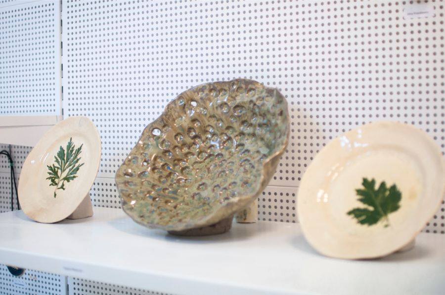 Zdjęcie promocyjne pracowni. Na zdjęciu prace wykonane na warsztatach ceramicznych. Ozdobne talerze ustawione na białej półce.