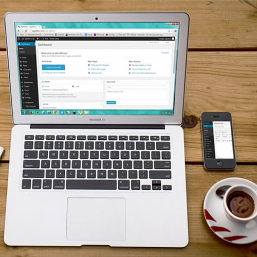 Zdjęcie: laptop stojący na stole, obok niego smartfon i filiżanka kawy