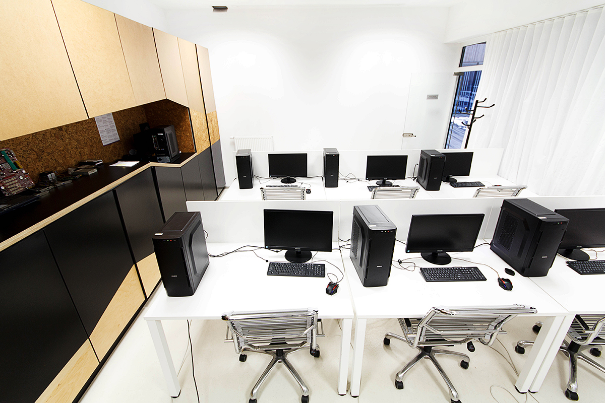 Na zdjęciu widoczna jest pracownia komputerowa. Biurka ustawione w dwóch rzędach, a na nich stojące komputery. 