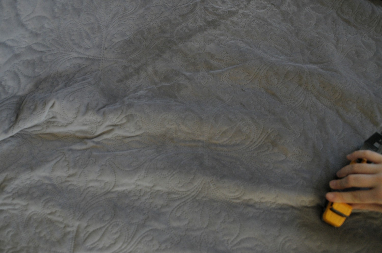 Prostokątne zdjęcie zdominowane ciemnoszarym odcieniem pościeli lub koca. W prawym dolnym rogu widać fragment dłoni trzymający żółty samochodzik, najpewniej w czasie zabawy. Foto. Joanna Kinowska