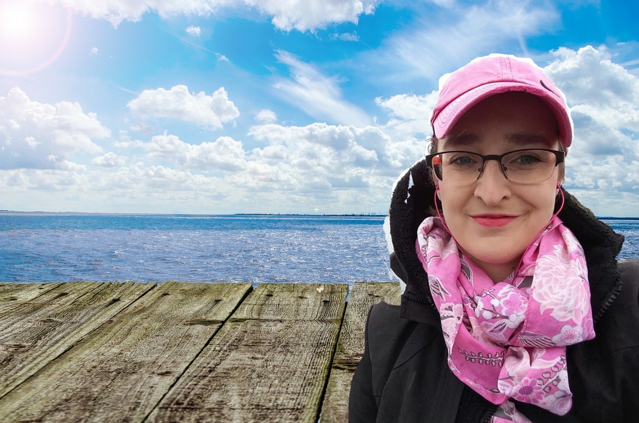 Na fotografii doklejony autoportret (selfie) do widoku na morze opisany na zdjęciu pierwszym. Bohaterka ma na sobie czarną kurtkę z kapturem, różowy szal, różową czapkę z daszkiem i okulary korekcyjne