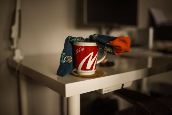 Na zdjęciu znajduje się kubek, a w nim umieszczona jest zwinięta skarpeta. Kubek stoi na białym stole pracowym, w oddali widać monitor. Fot. Agnieszka Mocarska