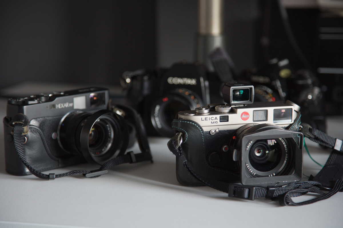 Zdjęcie przedstawia kilka aparatów fotograficznych i analogowych widzianych od przodu). W tle szare tło.
