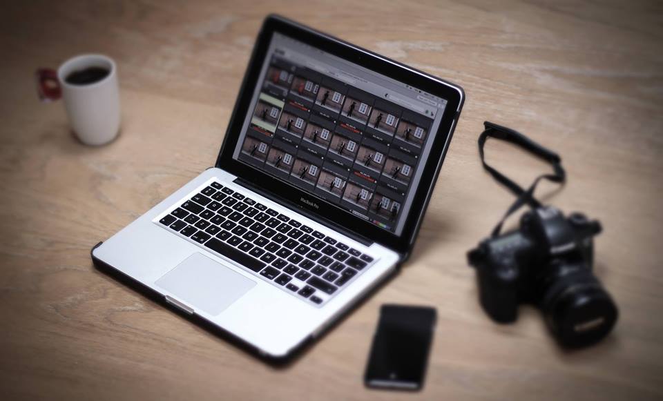 Zdjęcie promocyjne pracowni. Na zdjęciu laptop, aparat oraz kubek z kawą i telefon stoją na biurku.