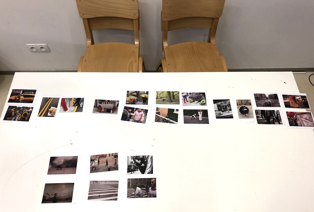 ujęcie przestawia biały stół sfotografowany od góry, na którym widać kilanaście zdjęć ułożonych w różnych grupach i kategoriach. Przy style dwa puste, drewniane krzesła. Białe ściany w tle.