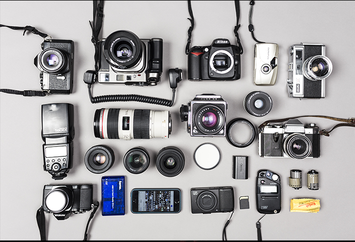 Na zdjęciu sprzęt fotograficzny rozłożony na białym blacie. Aparaty fotograficzne, obiektywy, lampy błyskowe etc.