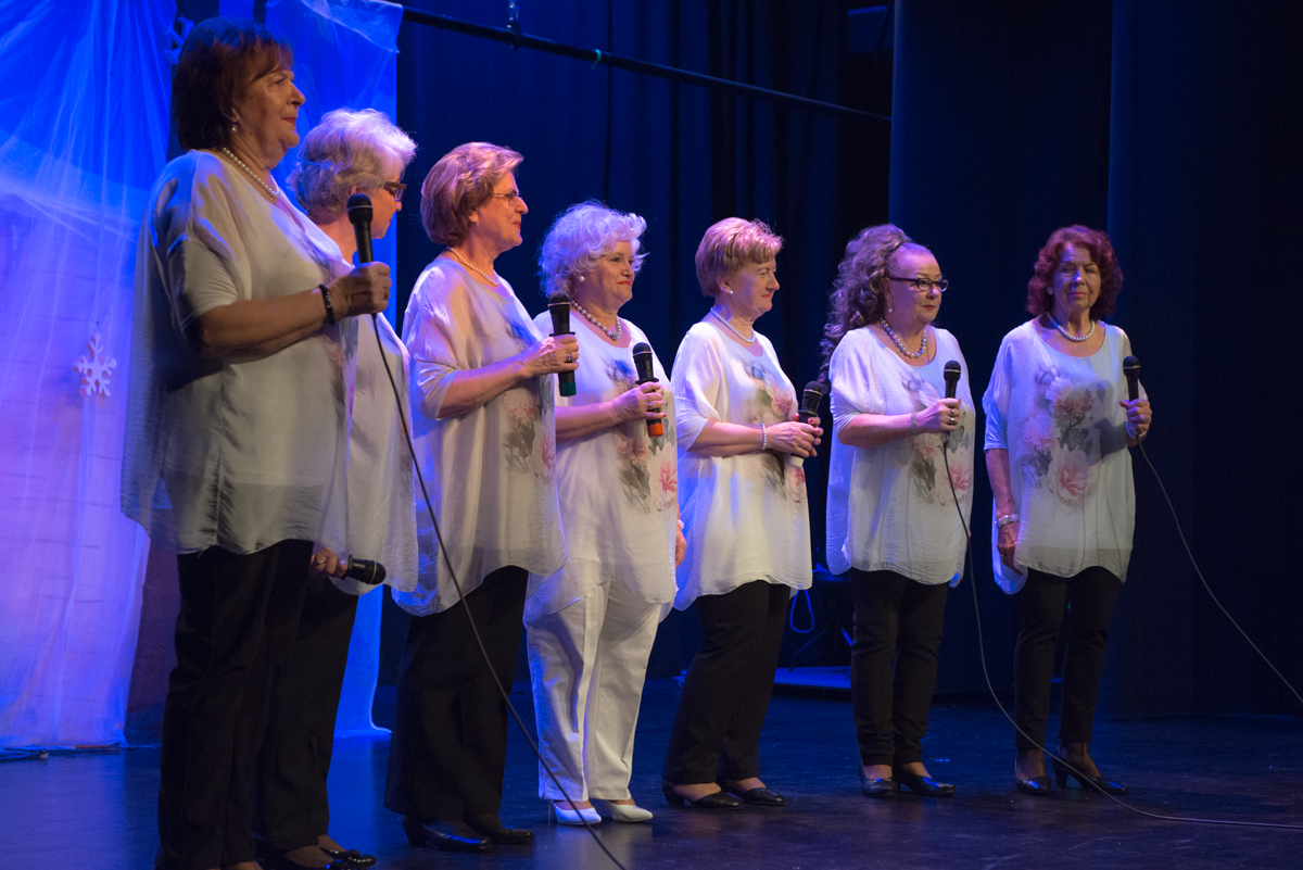 Zdjęcie promocyjne zespołu. Służewianki podczas próby gwiazdki w SDK. Artystki stoją na scenie z mikrofonami w rękach.