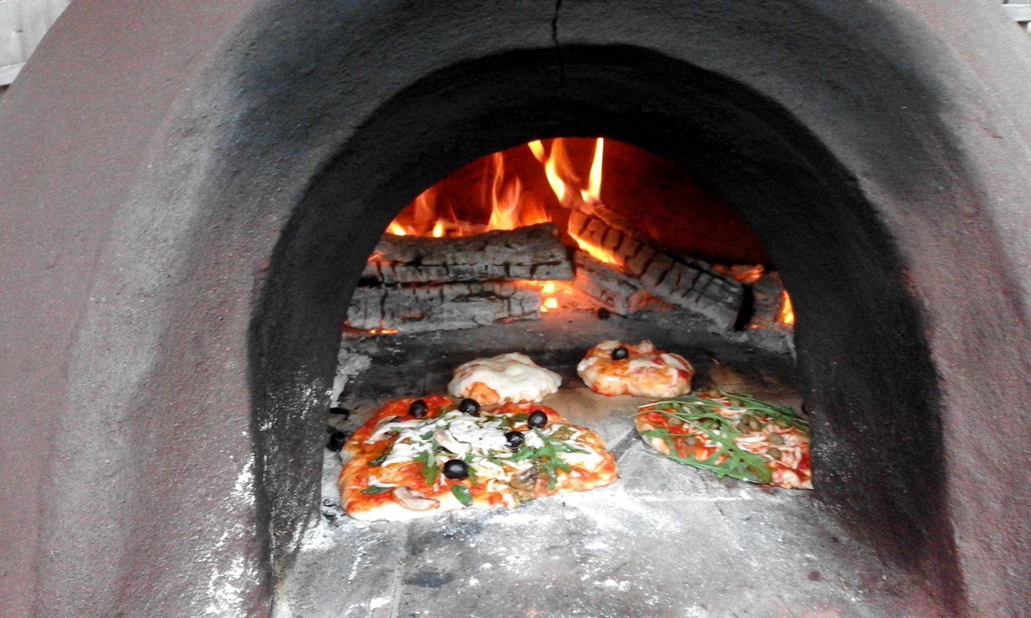 Ilustracja wprowadzenia przedstawiająca pieczące się pizze w piecu chlebowym. W tle palące się kawałki drewna