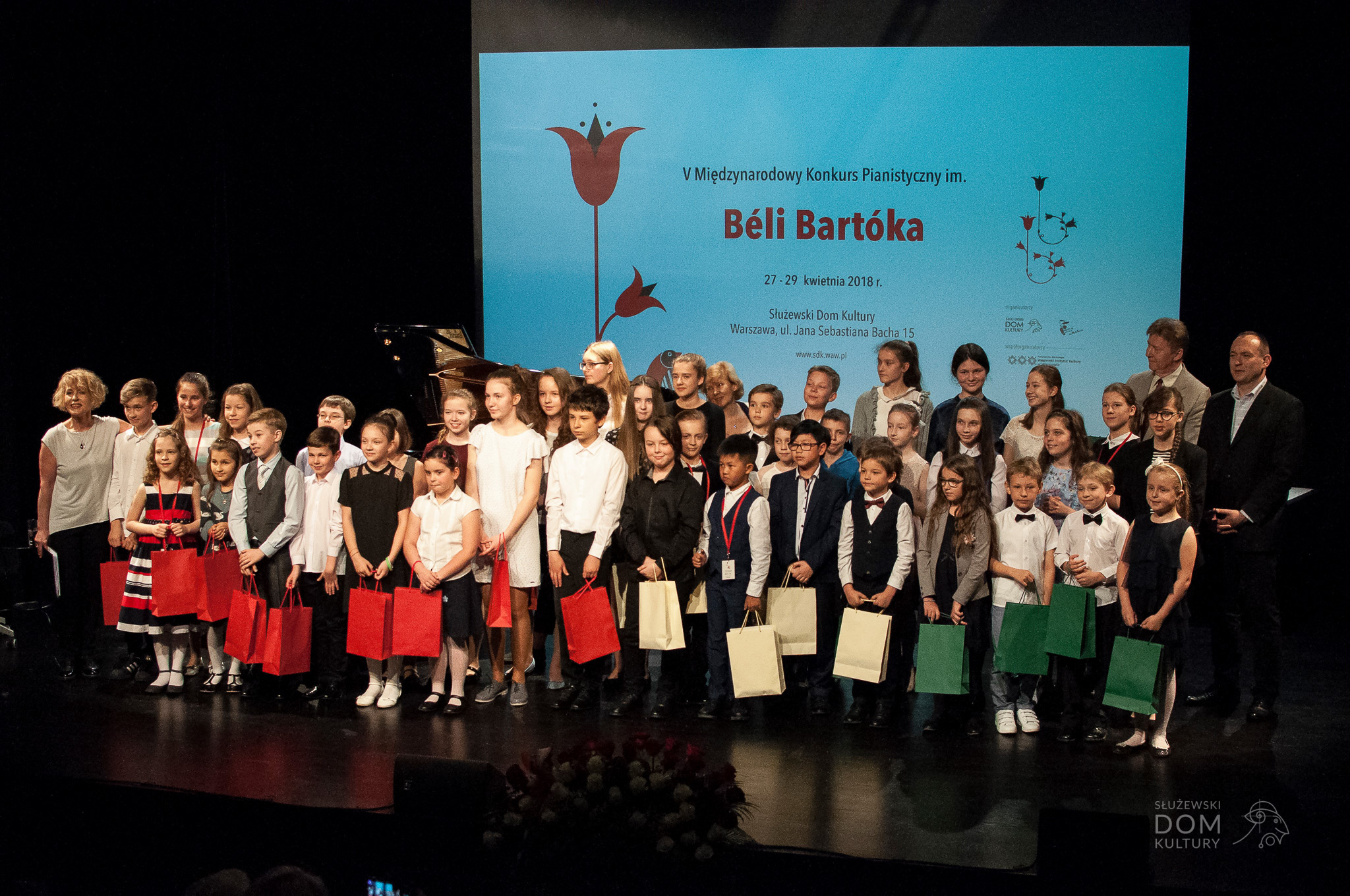 Zdjęcie przedstawia grupę uczestników poprzedniej edycji konkursu stojącą na scenie. Dzieci trzymają kolorowe torby z nagrodami w rękach