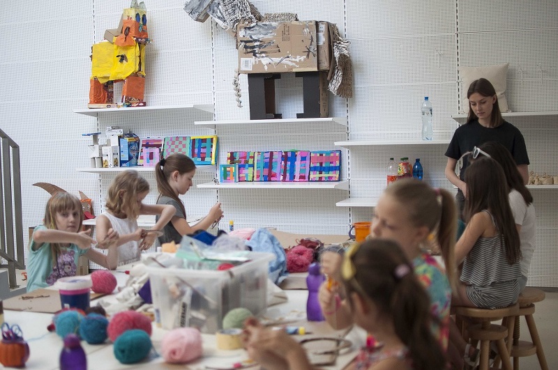 Dzieci podczas zajęć plastycznych. W tle prace uczestników i materiały warsztatowe