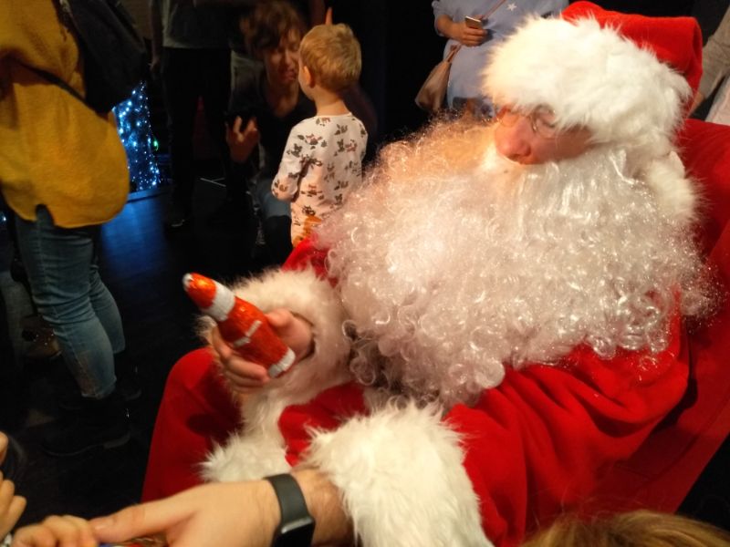 Na zdjęciu aktor w przebraniu Świętego Mikołaja rozdający prezenty. W tle uczestnicy imprezy (ustawieni tyłem)