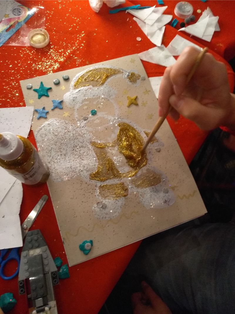 Zdjęcie przedstawia pracę plastyczną - Świętego Mikołaja pomalowanego w złote barwy. W tle czerwony obrus i przybry papiernicze