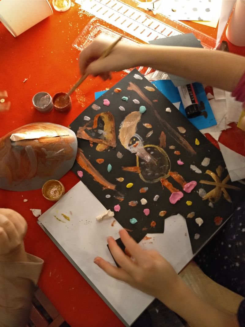 Zdjęcie przedstawia przygotowywaną pracę plastyczną z Mikołajem na środku kartki. W tle czerwony obrus i przybory papiernicze