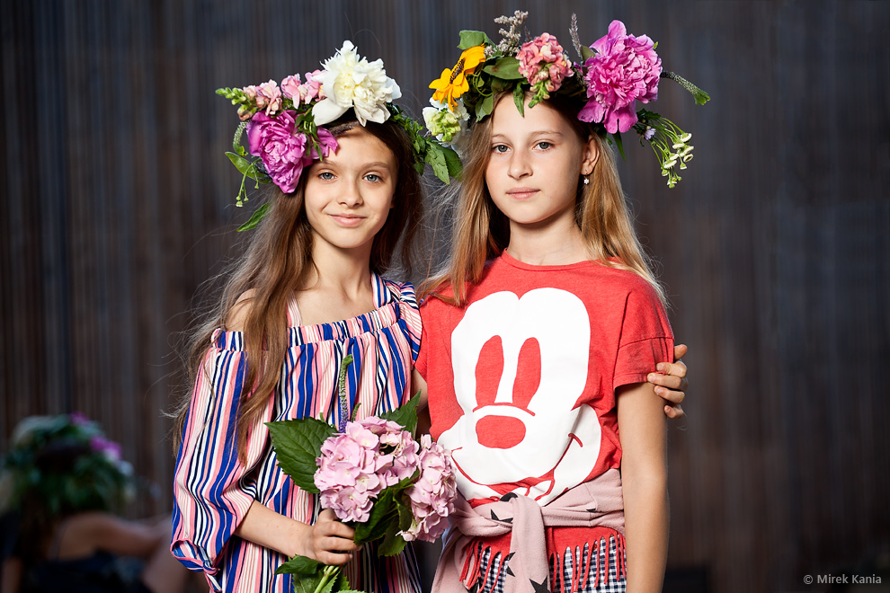 Zdjęcie przedstawia dwie dziewczynki w wiankach. W tle widać deski amfiteatru SDK>