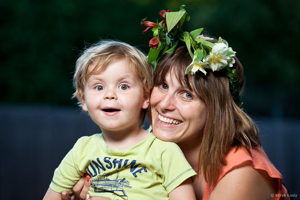 Na zdjęciu widać młodą kobietę w wianku przytulającą małego chłopca. W tle widać zieleń parku.