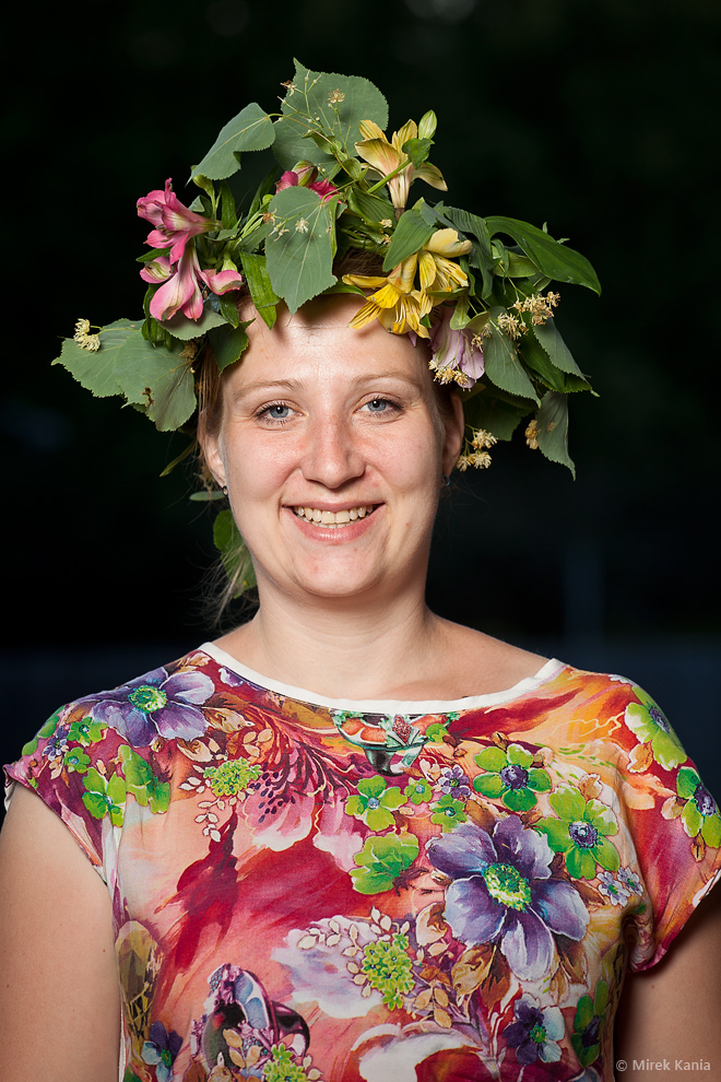 Na portretowym zdjęciu widoczna jest kobieta w wianku na ciemnym tle. 