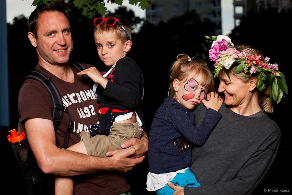 Zdjęcie przedstawia rodzinę. Rodzice trzymają na rękach dzieci. Tata trzyma chłopca, a mama córkę. 