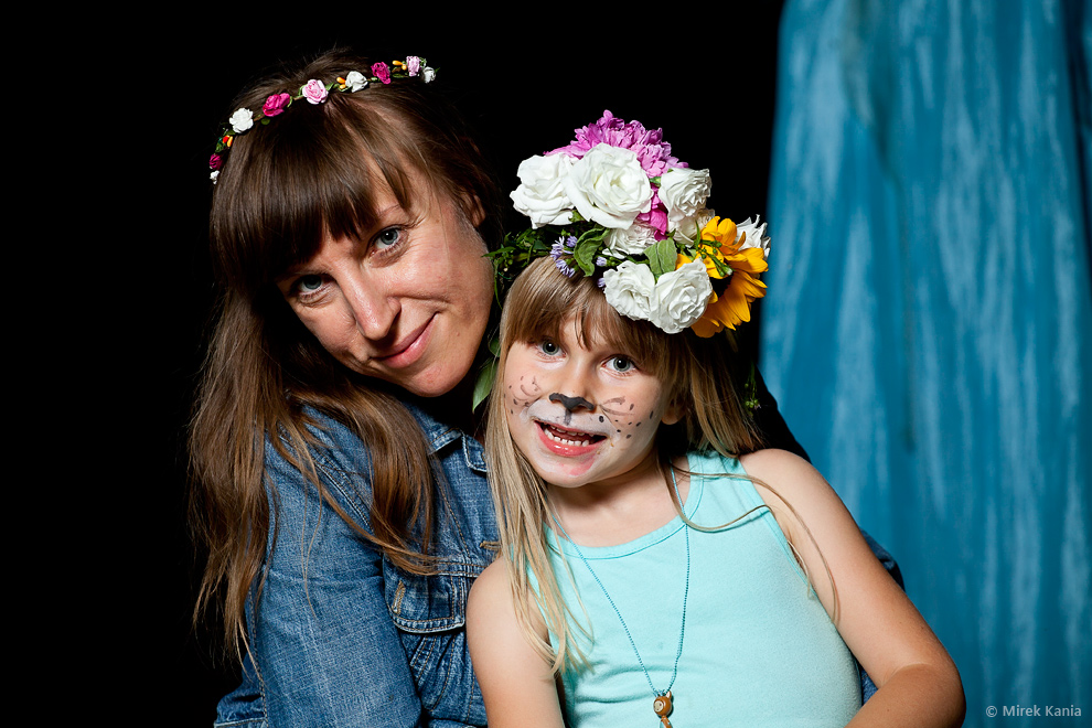 Na zdjęciu widoczna jest młoda kobieta w wianku, obok niej młoda dziewczynka również w wianku. Ciemne tło