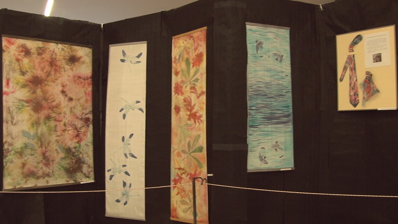 Na pierwszym planie prace od pracowni malowania na jedwabiu. W tle ciemne tło.