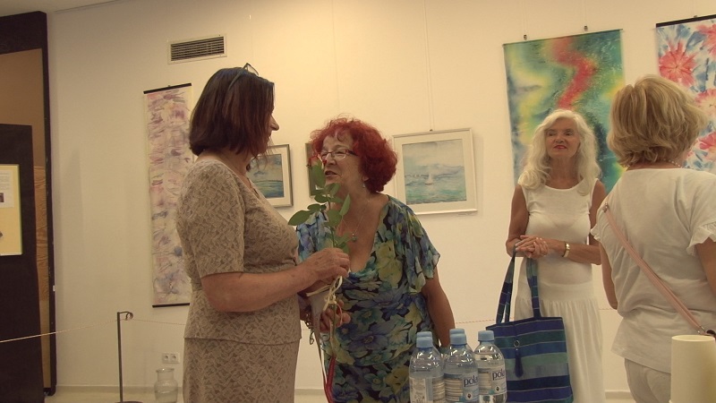 Uczestnicy wernisażu malowania na jedwabiu. W tle część wystawionych prac.