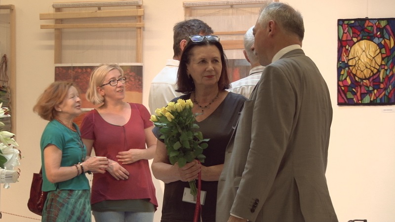 Na pierwszym kobieta z kwiatami i mężczyzna. W tle uczestnicy wernisażu i prace uczestników