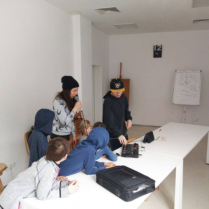 Na zdjęciu widoczna jest grupa osób stojących wokół stołu, na którym znajduje się sprzęt do beatboxu. Dziewczyna trzyma w ręku mikrofon. 