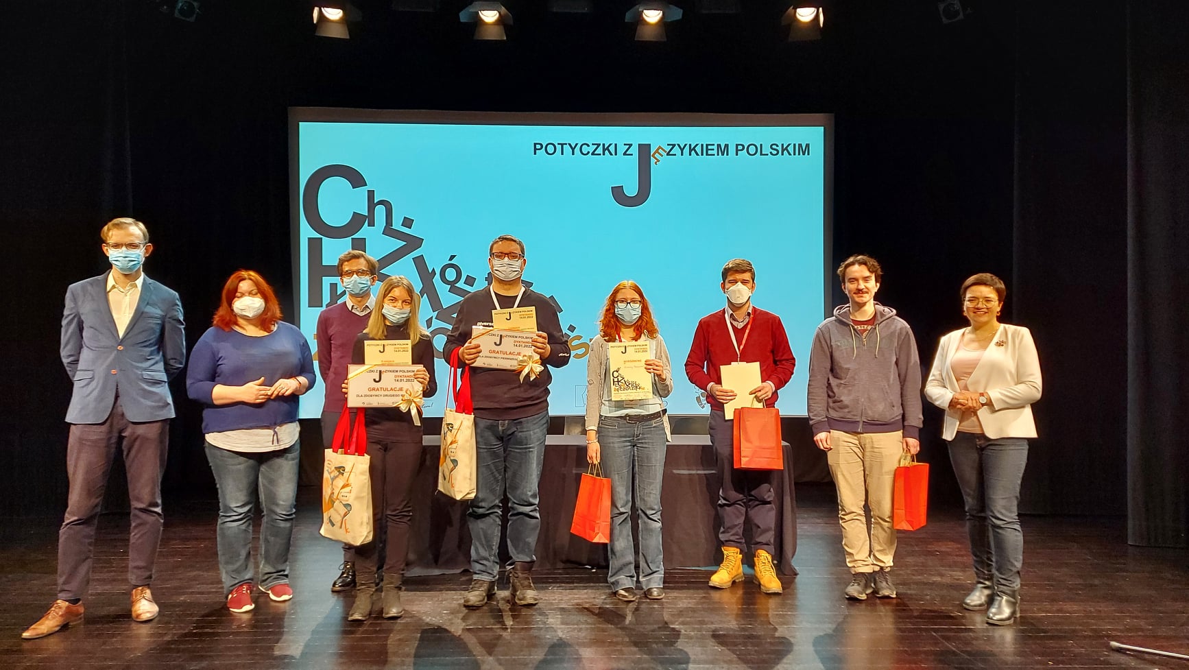 Na zdjęciu: wszyscy laureaci  dyktanda z nagrodami stojący na scenie. Za nimi ekran z grafiką identyfikującą wydarzenie.