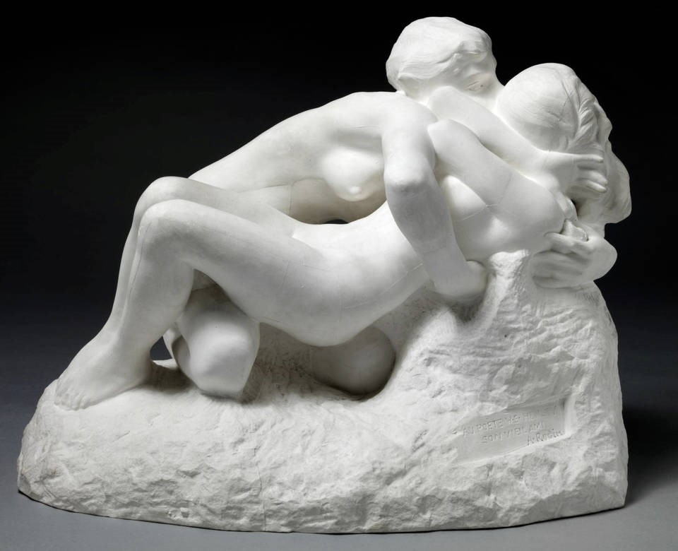 Fotografia przedstawa jasną rzeźbę Auguste'a Rodina, w której para nagich kochanków splata się w namiętnym pocałunku. Tło ciemne
