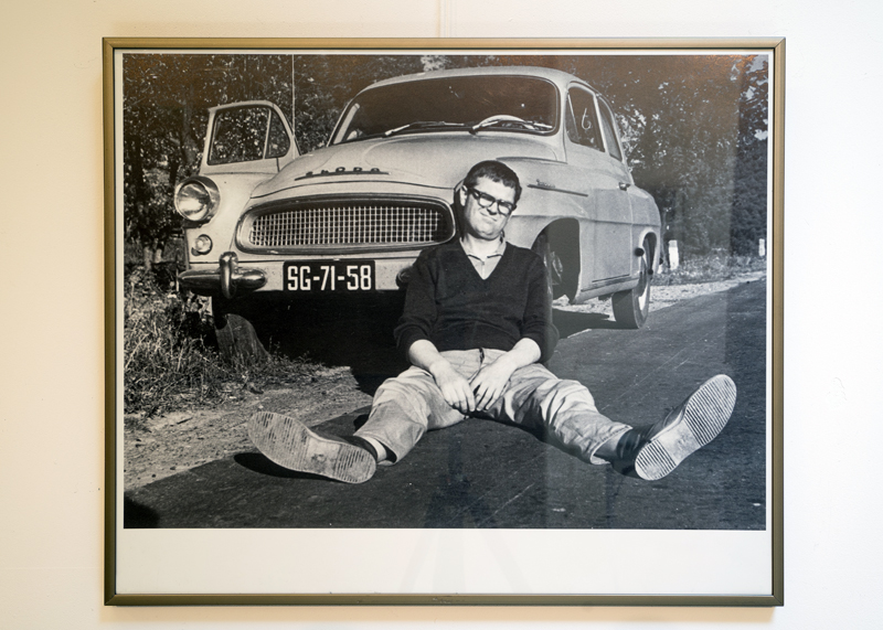 Zdjęcie ukazujące Zdzisława Beksińskiego przy swoim samochodzie, siedzącego na poboczu drogi asfaltowej.