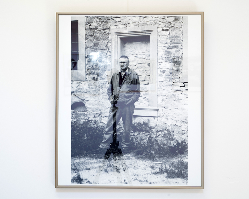 Fotografia ukazująca Zdzisława Beksińskiego stojącego przed sanockim zamkiem. W tle ściana murowana z blendą (ślepe okno).