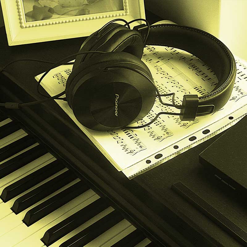 Kwadratowe zdjęcie fragmentów klawiatury fortepianu, nut i leżących na nich słuchawek