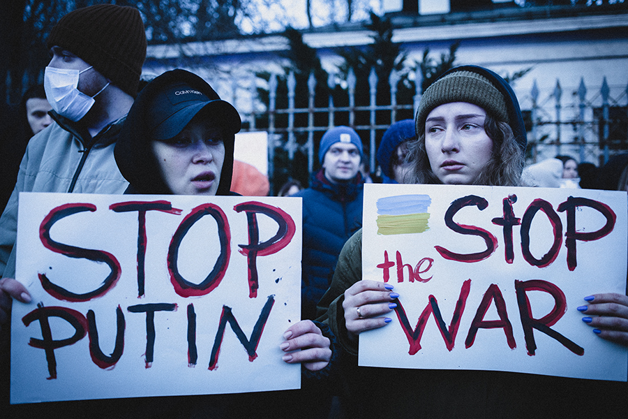 Fot.. Agata Kubis / Na zdjęciu fragment protestu ulicznego: na pierwszym planie dwie kobiety trzymające przed sobą w dłoniach plansze. Na jednej (po lewej) odręczny napis "STOP PUTIN". Na drugiej (po prawej) "STOP the WAR". Za postaciami fragment ogrodzenia i budynku oraz inne osoby.