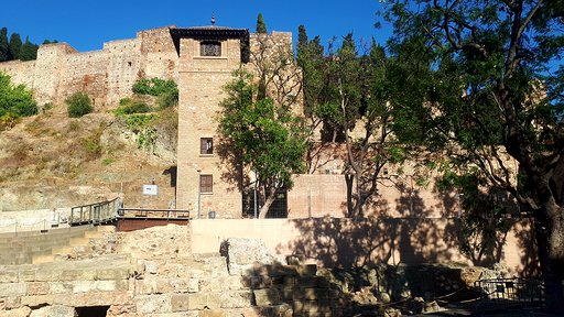 Na zdjęciu znajduje się fragment krajobrazu Malagi. Widoczne starodawna budowla na wzniesieniu. W tle czyste, błękitne niebo. 