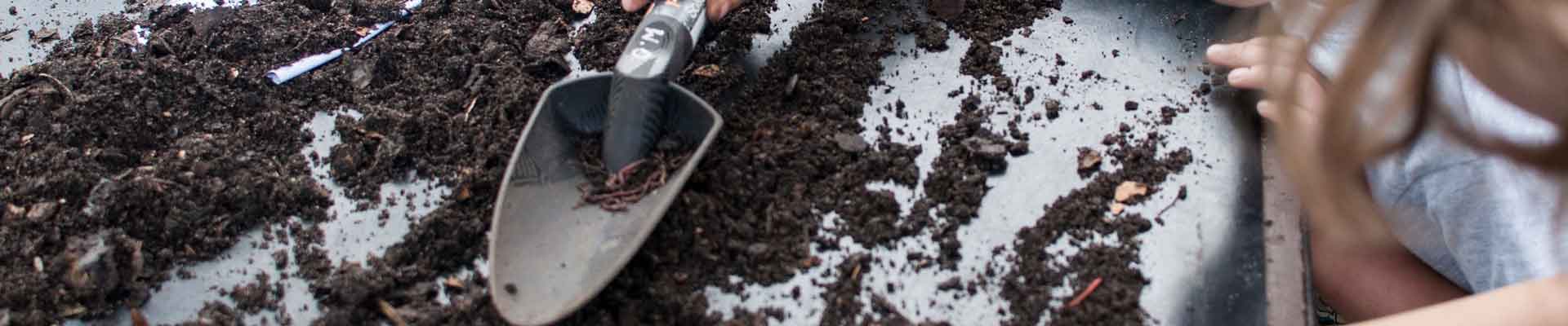 Na zdjęciu dwoje dzieci pochylone z łopatką ogrodniczą nad rozsypaną na białym podkładzie ziemią. Fot.: Dominika Dzieniszewska