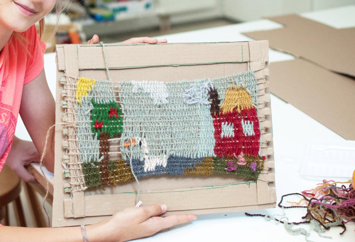 Zdjęcie pracy uczestnika/czki waszrtatów plastycznych. W centralnej części kadru kolorowa wyplatanka ze sznrurków, stworzona na drewnianej, roboczej ramie. fot.D. Dzieniszewska