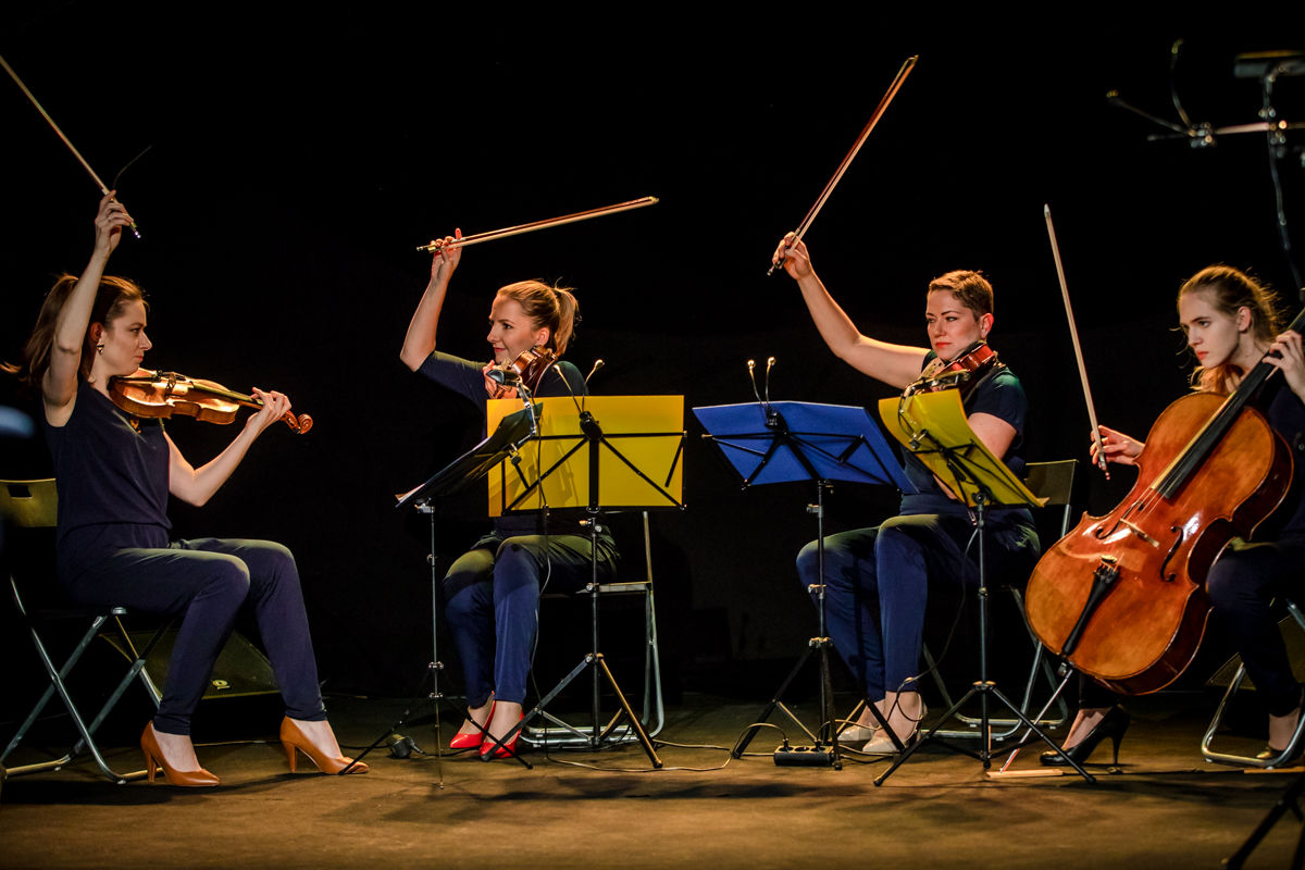 Na zdjęciu Kwartet Polonika na scenie: cztery kobiety z instrumentami smyczkowymi przy pulpitach nutowych, Fot. Kasia Chnura.