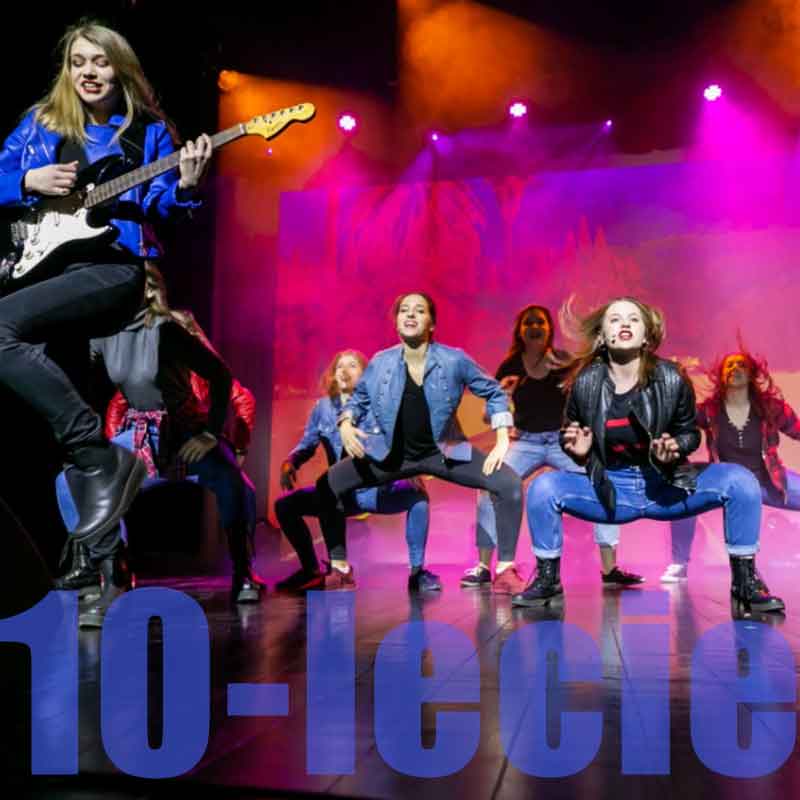 Zdjęcie:  grupa kilku dziewcząt w tanecznym ruchu na scenie. Dziewczyna na pierwszym planie podskakuje z gitarą w rękach. Fot. Weronika Pawłowska - Ciągło