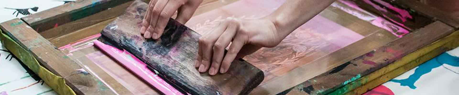 Ręce postaci wykonującej raklą odbitkę na sicie do sitodruku. Fot. Dominika Dzieniszewska