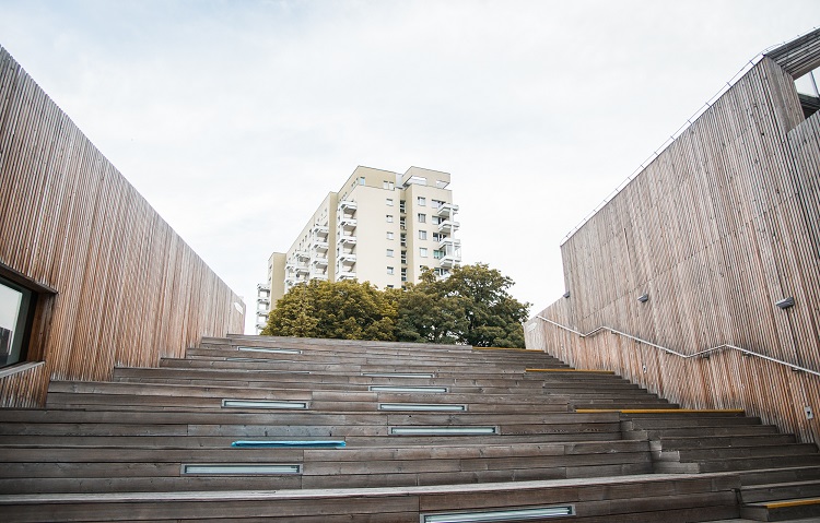 Na zdjęciu widać służewskie bloki przy ul. Bacha widziane od strony amfiteatru SDK. Bloki otoczone są drewnianą elewacją. Do zdjęcia wykorzystaną perpektywę żabią.