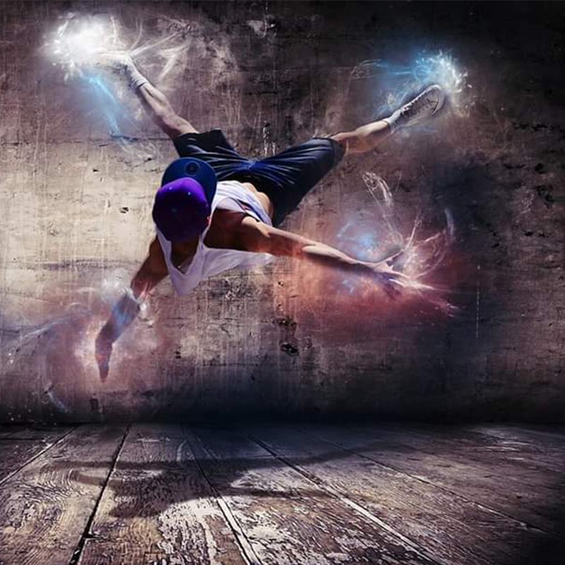 Na zdjęciu mężczyzna wykonujący ewolucje w powietrzu. Ubrany w luźny strój, białą podkoszulkę, krótkie niebieskie spodnie oraz czapkę. Przy jego dłoniach oraz stopach znajdują się efekty świetlne.