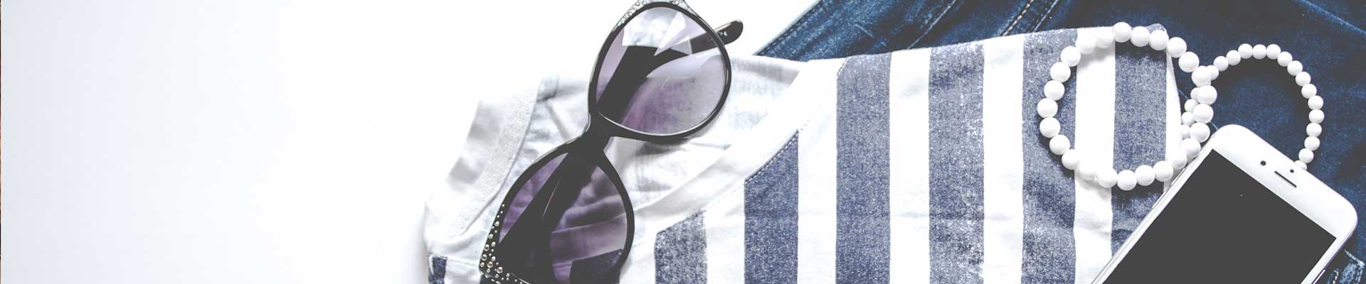 Poziome zdjęcie. Zestaw ubrań w odcieniach granatu na nich smartfon i perły.