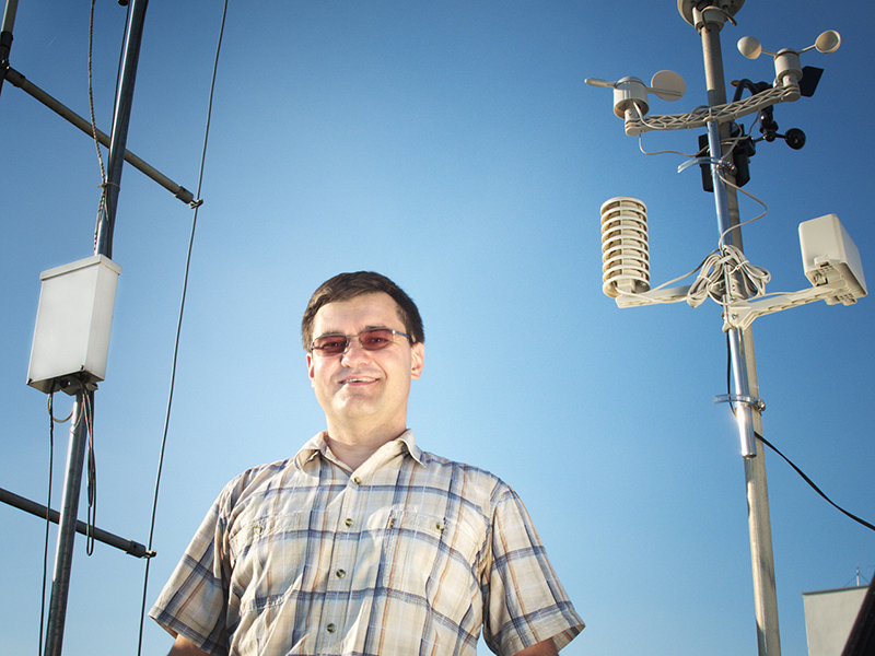 Na zdjęciu: Marcin Popkiewicz obok urządzeń pomiarowych na tle bezchmurnego nieba