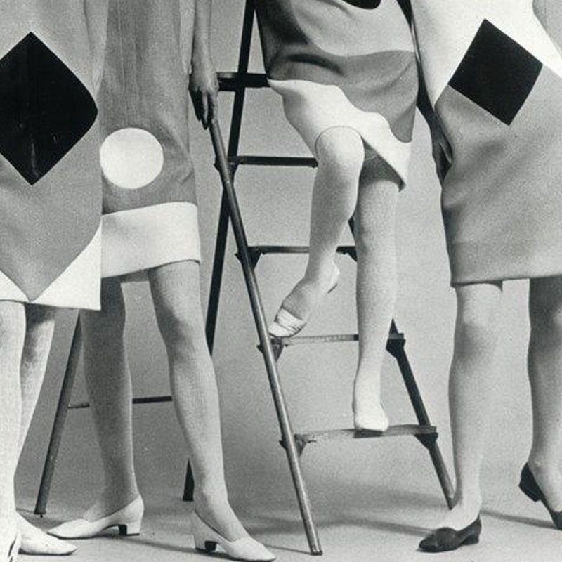 Na starym zdjęciu nogi czterech kobiet ubranych w sukienki z lat pięćdziesiątych. Pomiędzy Paniami stoi drabina.