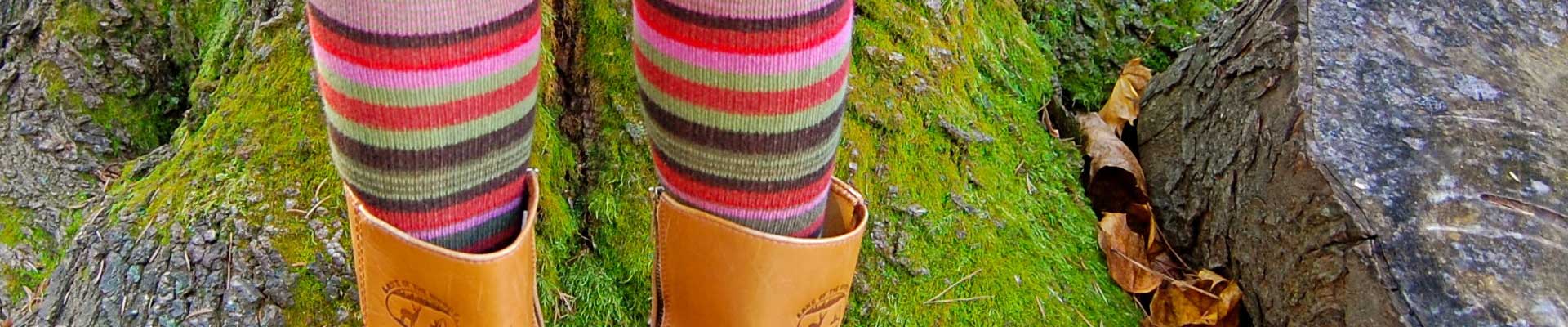 Kwadratowe zdjęcie: Na tle omszałego drzewa dziecięce nogi w kolorowych podkolanówkach.